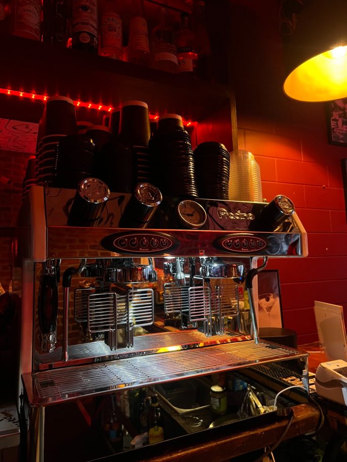Coffee machine with stacked cups, illuminated by warm red lighting.