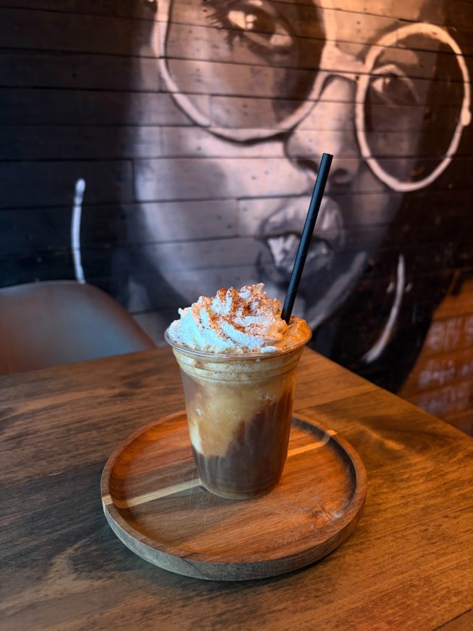 Iced coffee topped with whipped cream and caramel, served on a wooden tray.